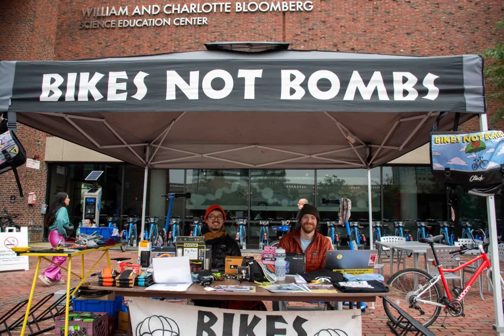 Two men sitting under a tent that says "Bikes Not Bombs"